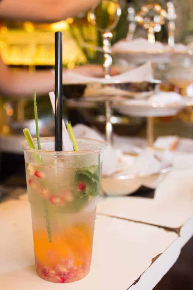 Plastic cup with a colorful cocktail, garnished with herbs and fruit, on a table at a bar or restaurant.