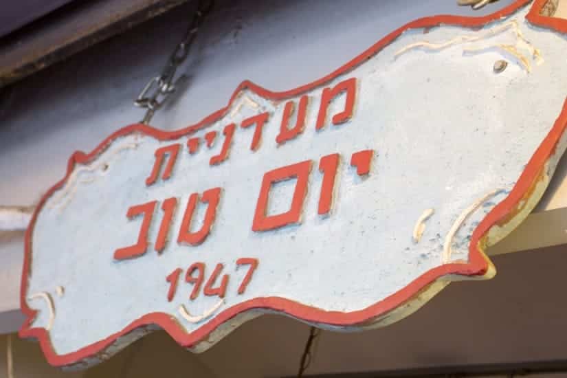 A wooden sign with Hebrew text and the year 1947, painted red on a white background with a red border.