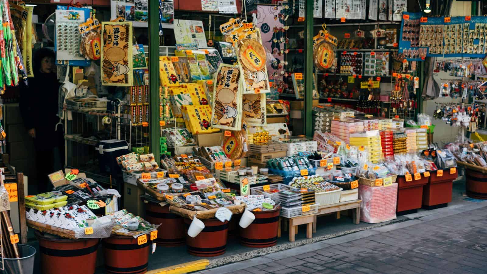 Street market stall in Japan selling colorful souvenirs, snacks, and trinkets, with price tags on display.