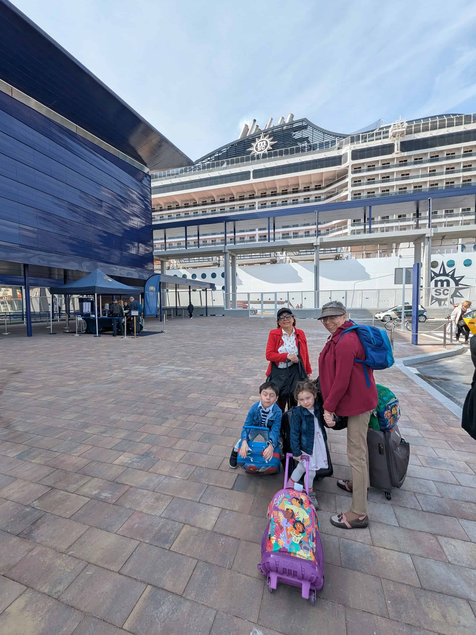 Family with suitcases stands outside a cruise ship terminal, ready to board a large cruise ship and looking forward to experiencing MSC Fantasia dining onboard.