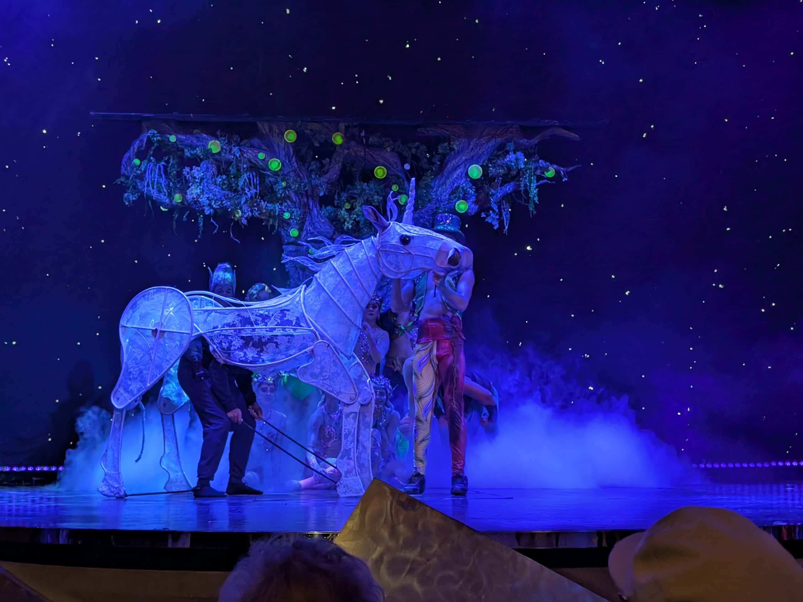 Performers on stage with a luminous horse puppet, mystical tree, and starry backdrop under blue lighting bring the magic of MSC Cruise Fantasia to life.