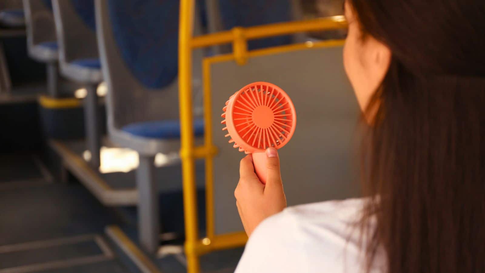 A person on a bus holds a small, pink handheld fan, facing away from the camera.
