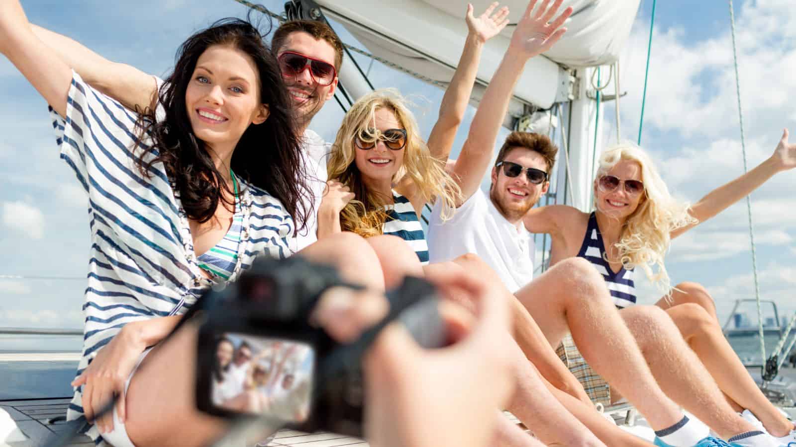 Five friends in striped shirts smiling and waving while sitting on a boat, posing for a photo on a sunny day.