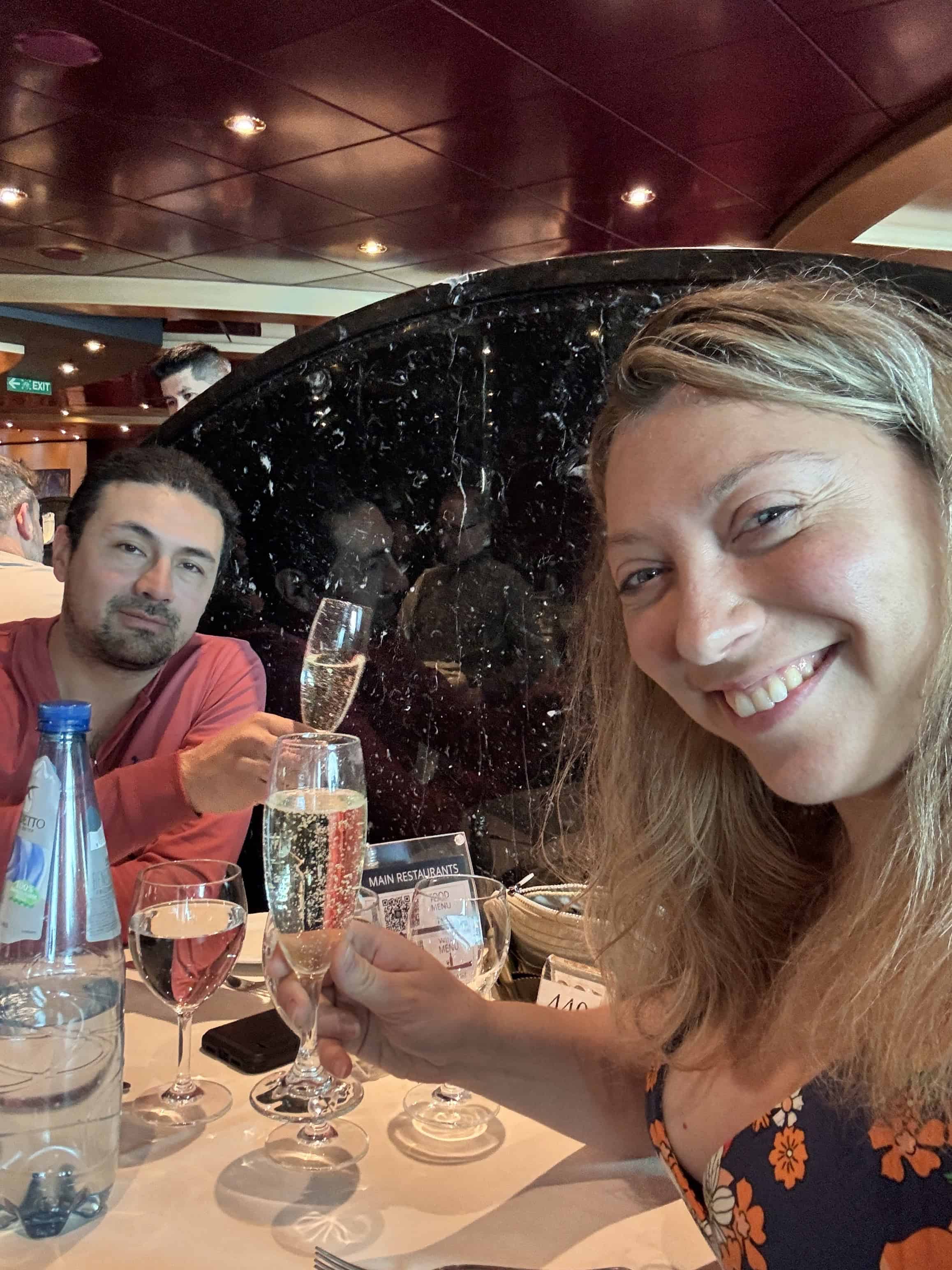 A woman and man smile and toast with champagne at a restaurant table with drinks and water.
