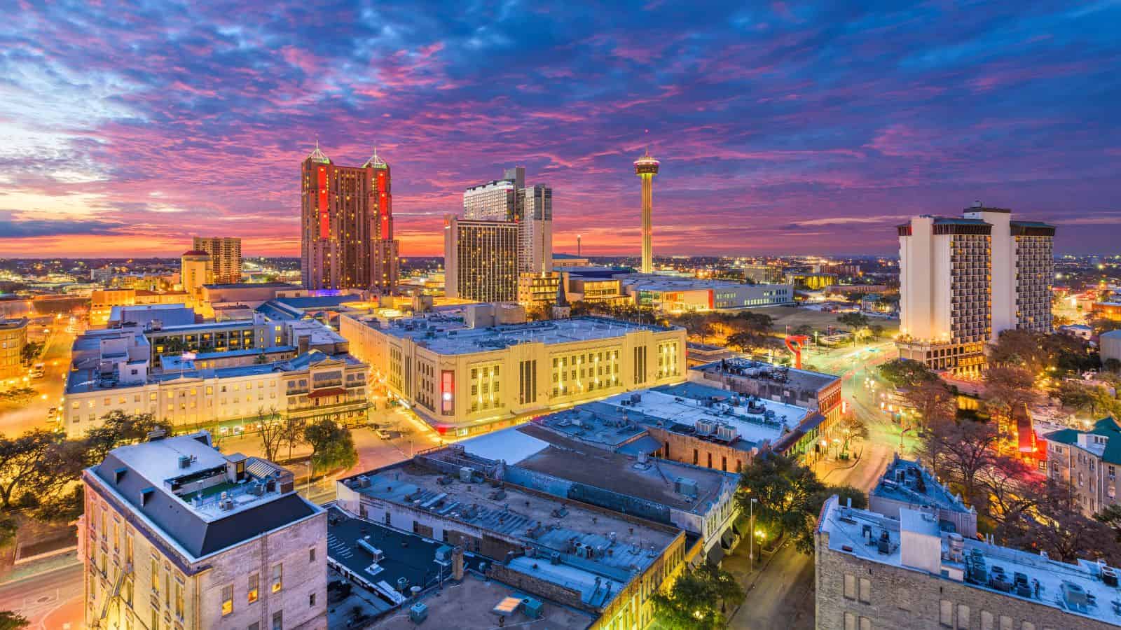 Downtown San Antonio skyline at sunset with colorful clouds and city lights illuminating the buildings, highlighting one of the U.S. cities actively addressing water shortage concerns.