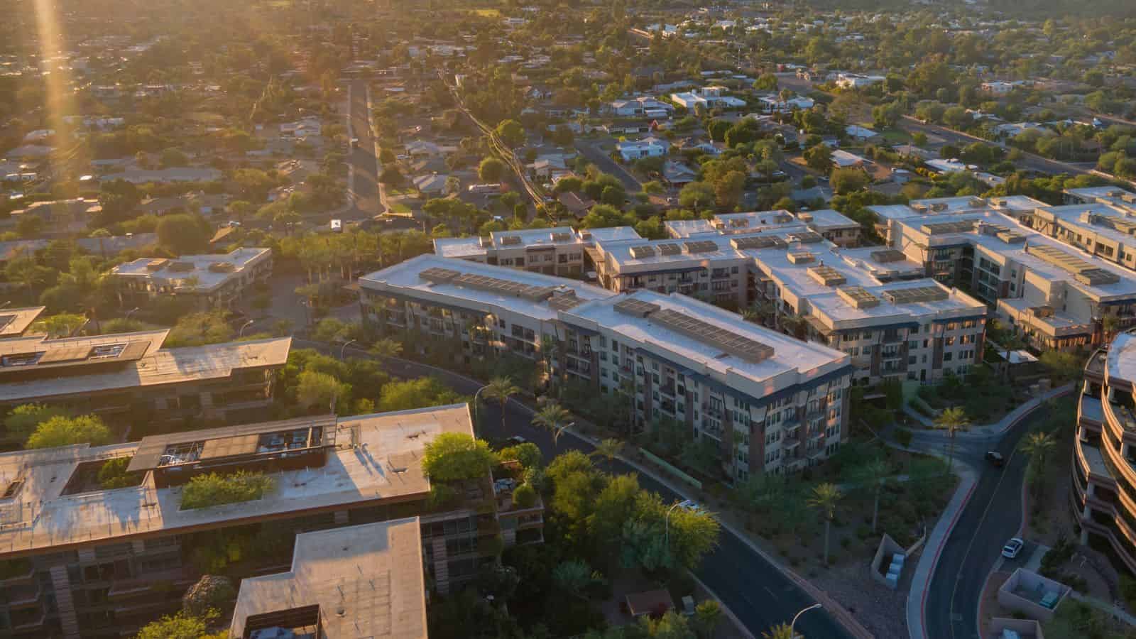 Aerial view of modern apartment buildings and suburban homes at sunset in U.S. cities, with trees, roads, and hints of ongoing water shortage challenges visible.