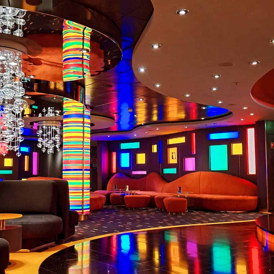 Colorful modern lounge with neon lights, round orange couches, and reflective surfaces—evoking the vibrant ambiance of MSC Fantasia dining.