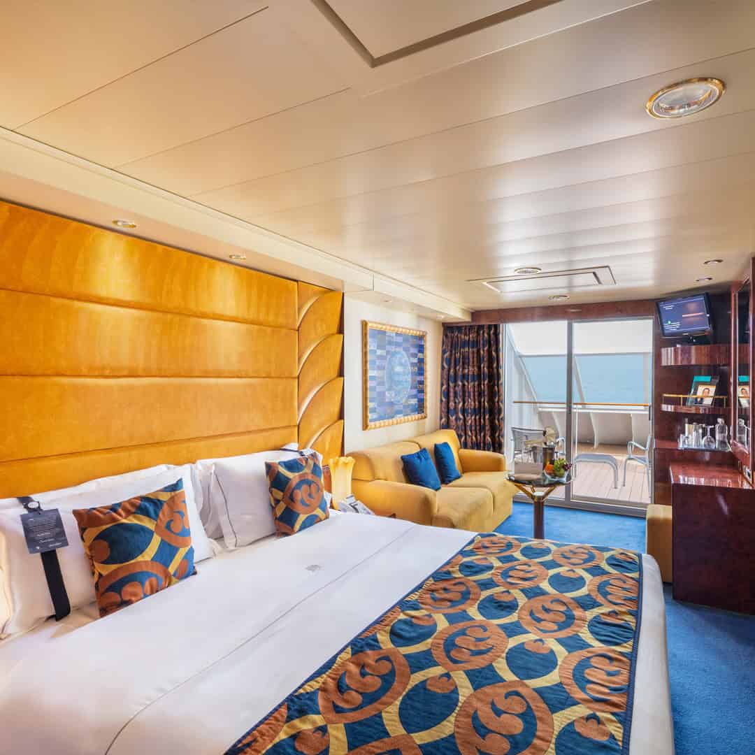 Luxurious cruise ship cabin with a large bed, sofa, TV, and private balcony overlooking the sea—just steps away from world-class MSC Fantasia dining experiences.