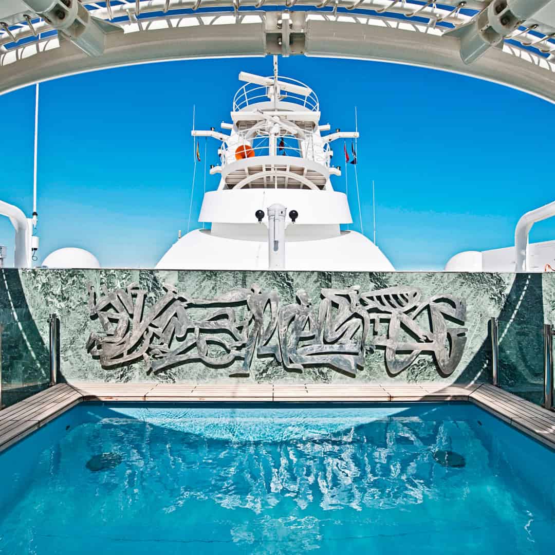 A luxury yacht pool with clear blue water and modern art behind, under a bright blue sky, evokes the elegance of MSC Fantasia Dining at sea.