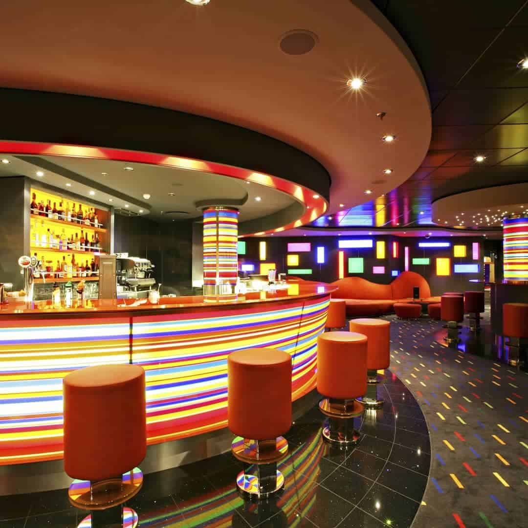 A vibrant, modern bar on MSC Fantasia Dining with colorful striped lights, red stools, and illuminated wall panels.