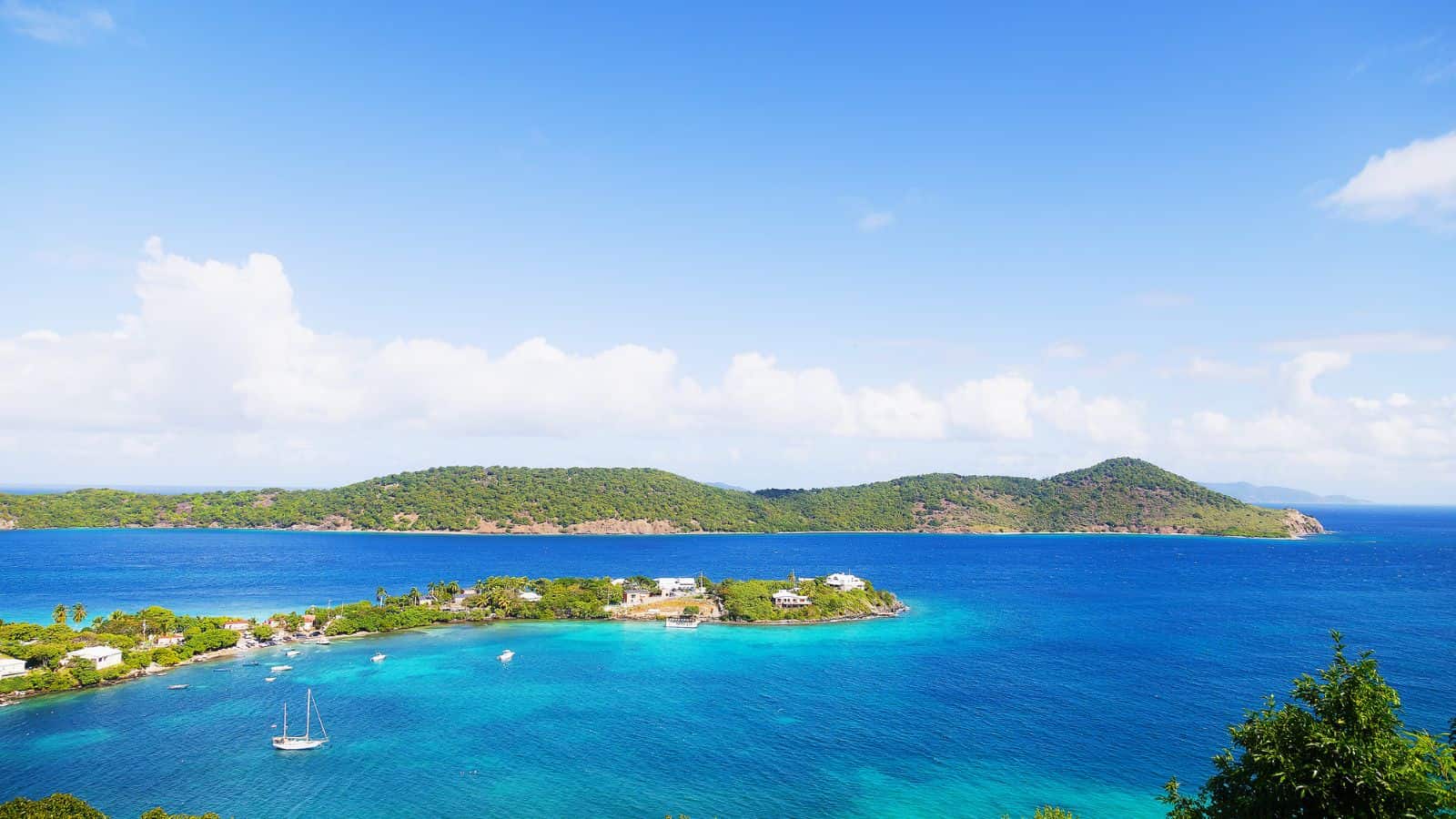 Aerial view of a tropical island with lush greenery, blue water, boats, and houses under a clear sky.