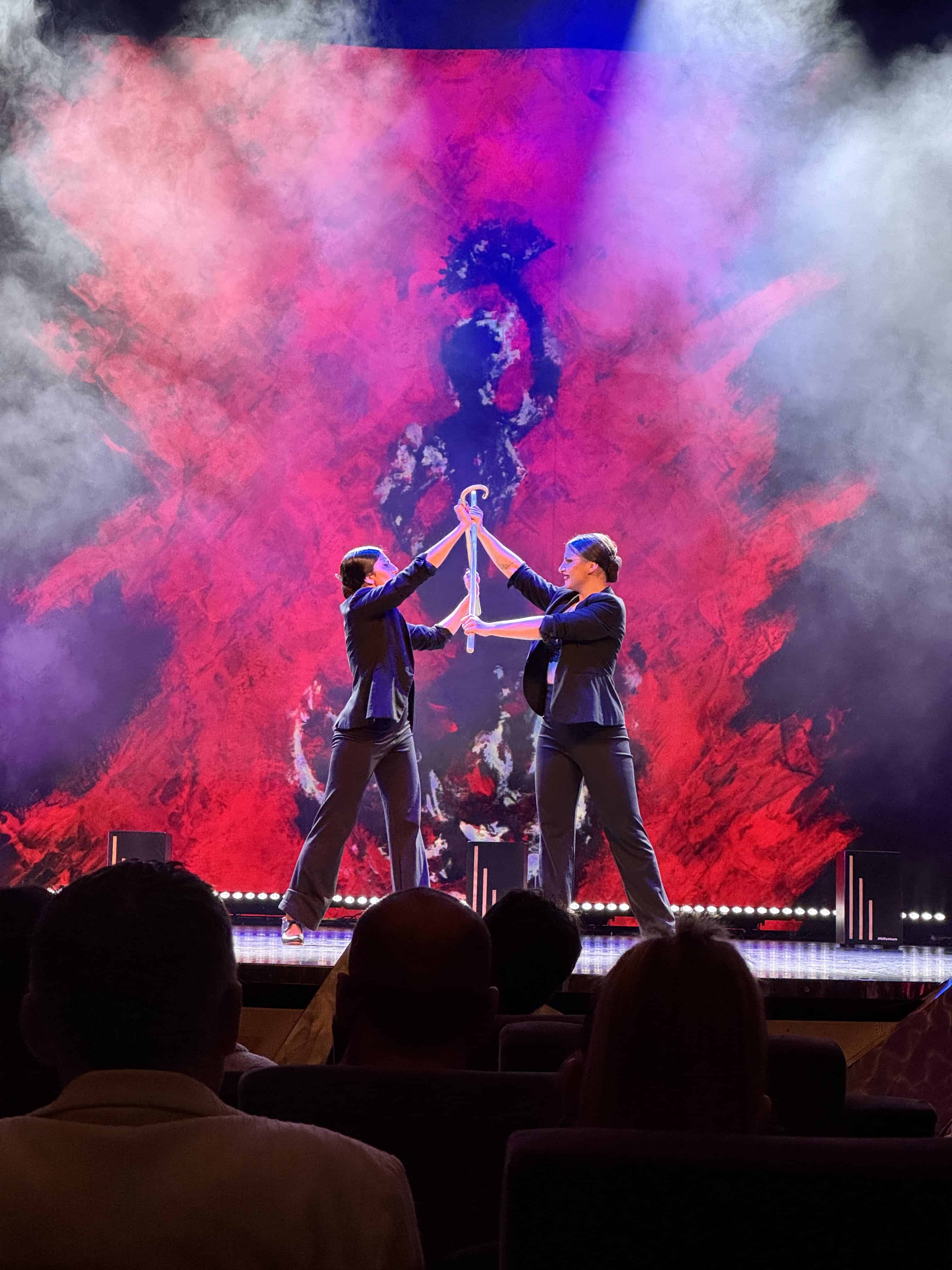 Two performers in suits hold glowing sticks onstage, with red and black smoke effects in the background—one of the many dazzling shows that make an MSC Fantasia Cruise a memorable family cruise experience.