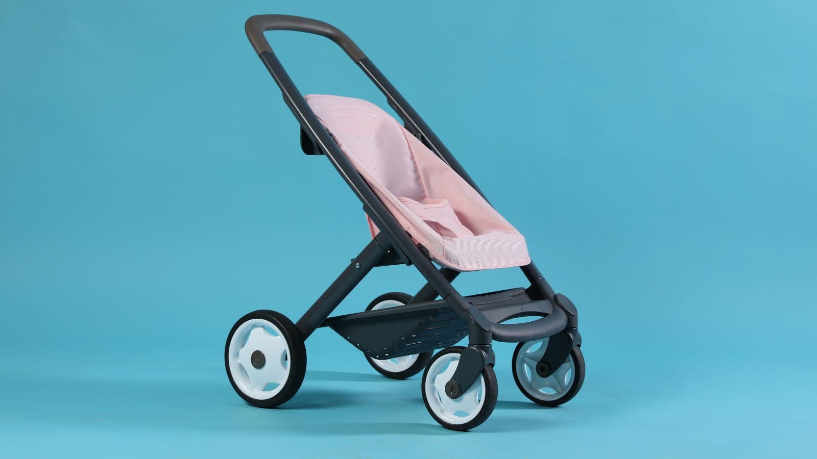 A modern stroller with a pink fabric seat, black frame, and four white wheels is positioned against a plain blue background. Strollers are among the commonly lost items found at U.S. airports, often left behind by busy travelers.