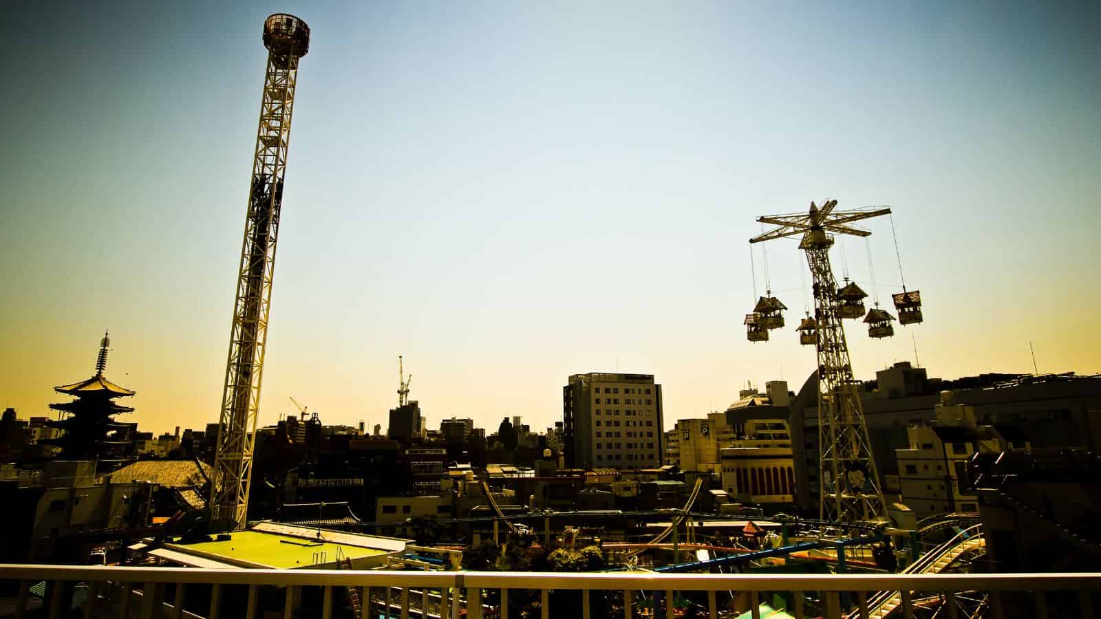 Amusement park rides with a city skyline in the background under a clear, bright sky.