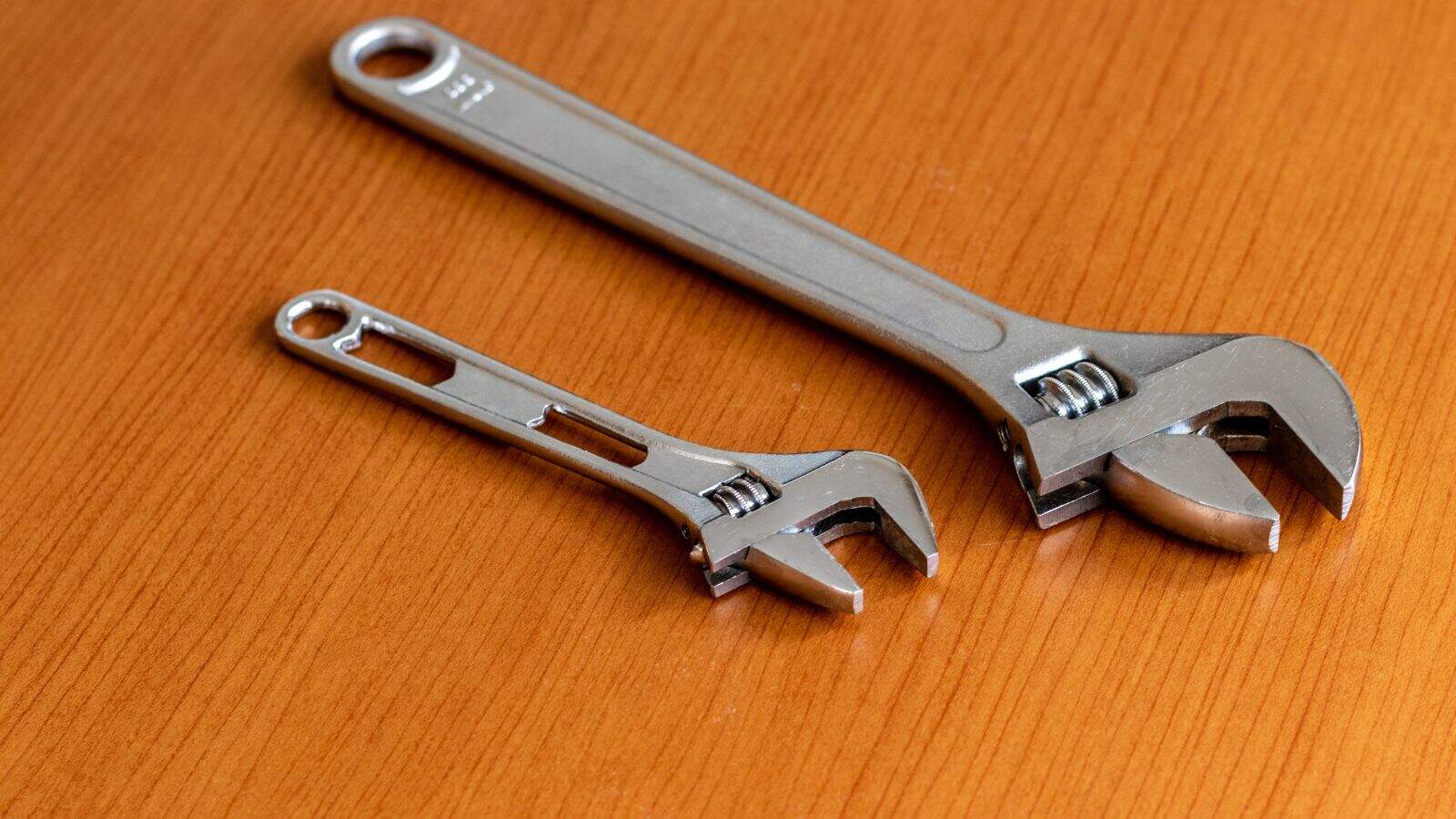 Two adjustable wrenches, one small and one large, are placed on a wooden surface&mdash;similar to confiscated items often held by airport security due to restricted tools. Both feature open-ended jaws and screw mechanisms for adjusting width.