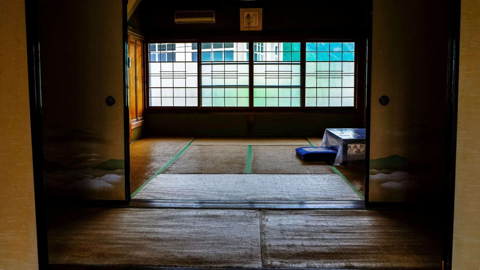 A traditional Japanese room with tatami mats, shoji screens, and a low table with a cushion.