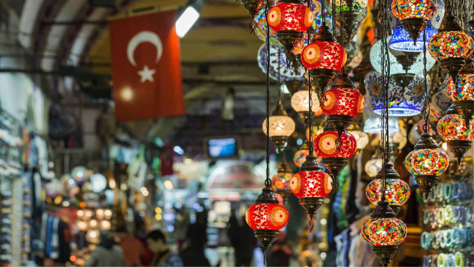 Colorful mosaic lamps hanging in a bustling Turkish bazaar, with a Turkish flag in the background.