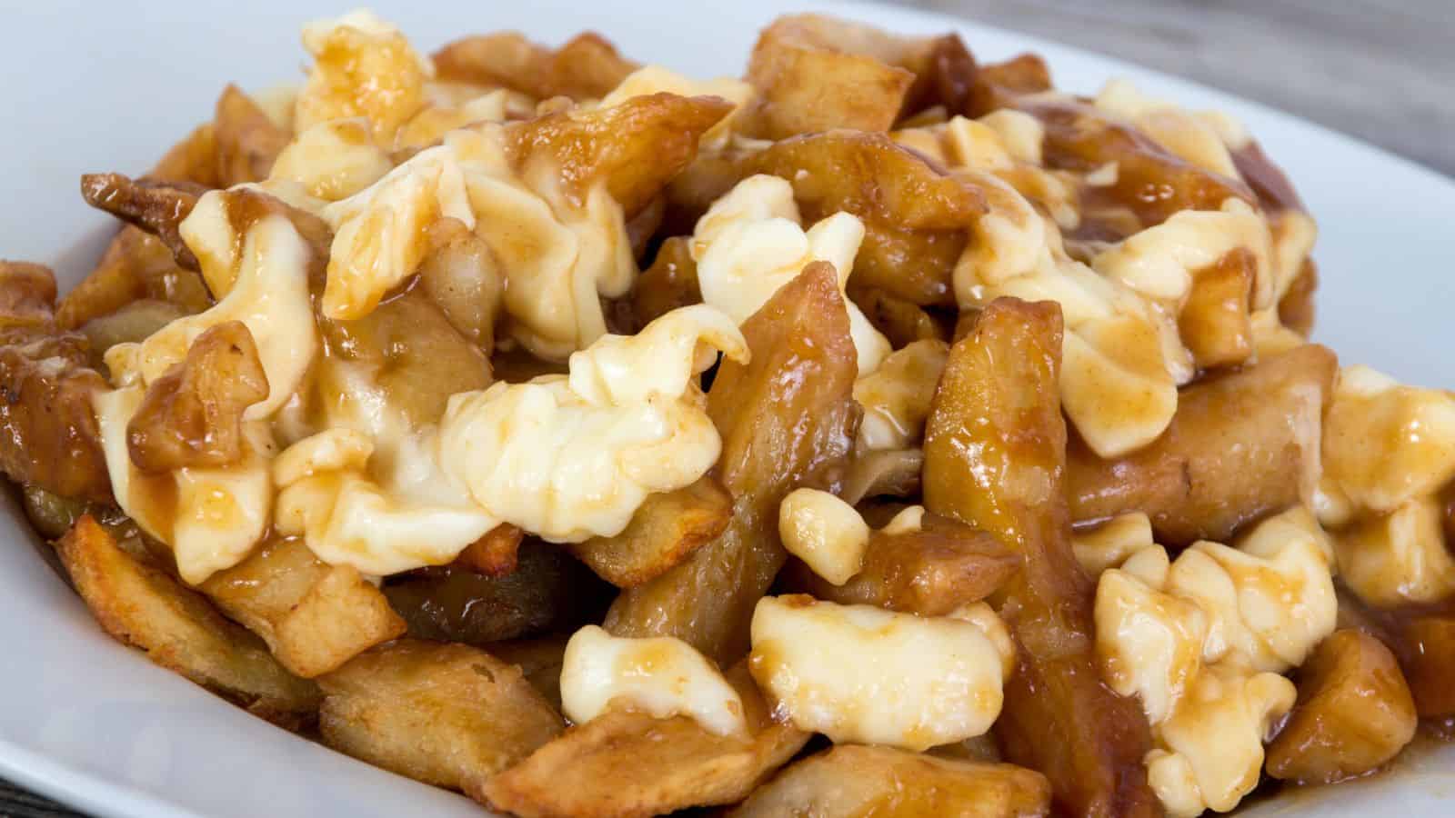 A close-up of a plate of poutine, featuring golden French fries topped with white cheese curds and covered in brown gravy.