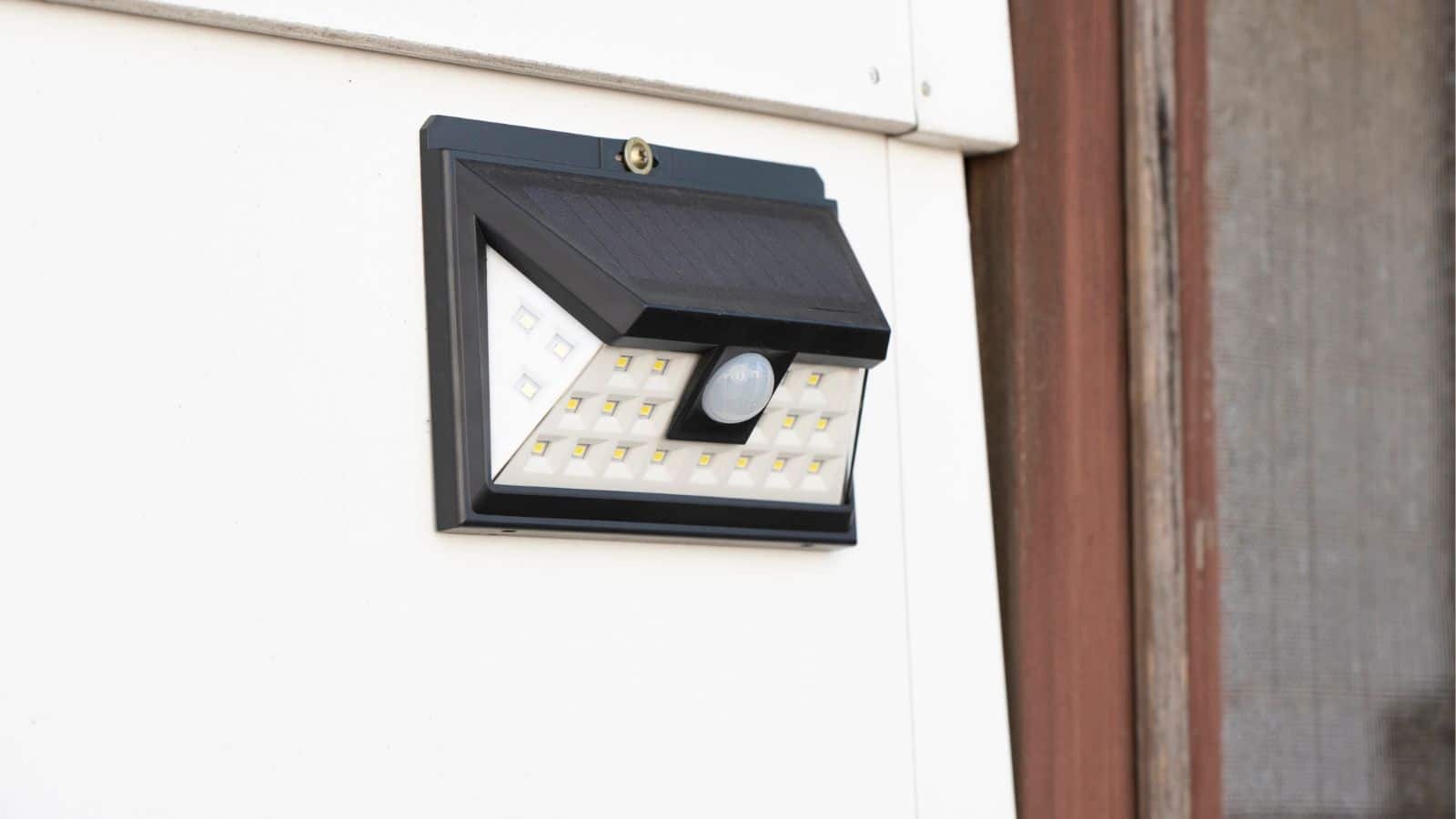 Solar-powered LED outdoor wall light with motion sensor mounted on a white wall next to a door frame.