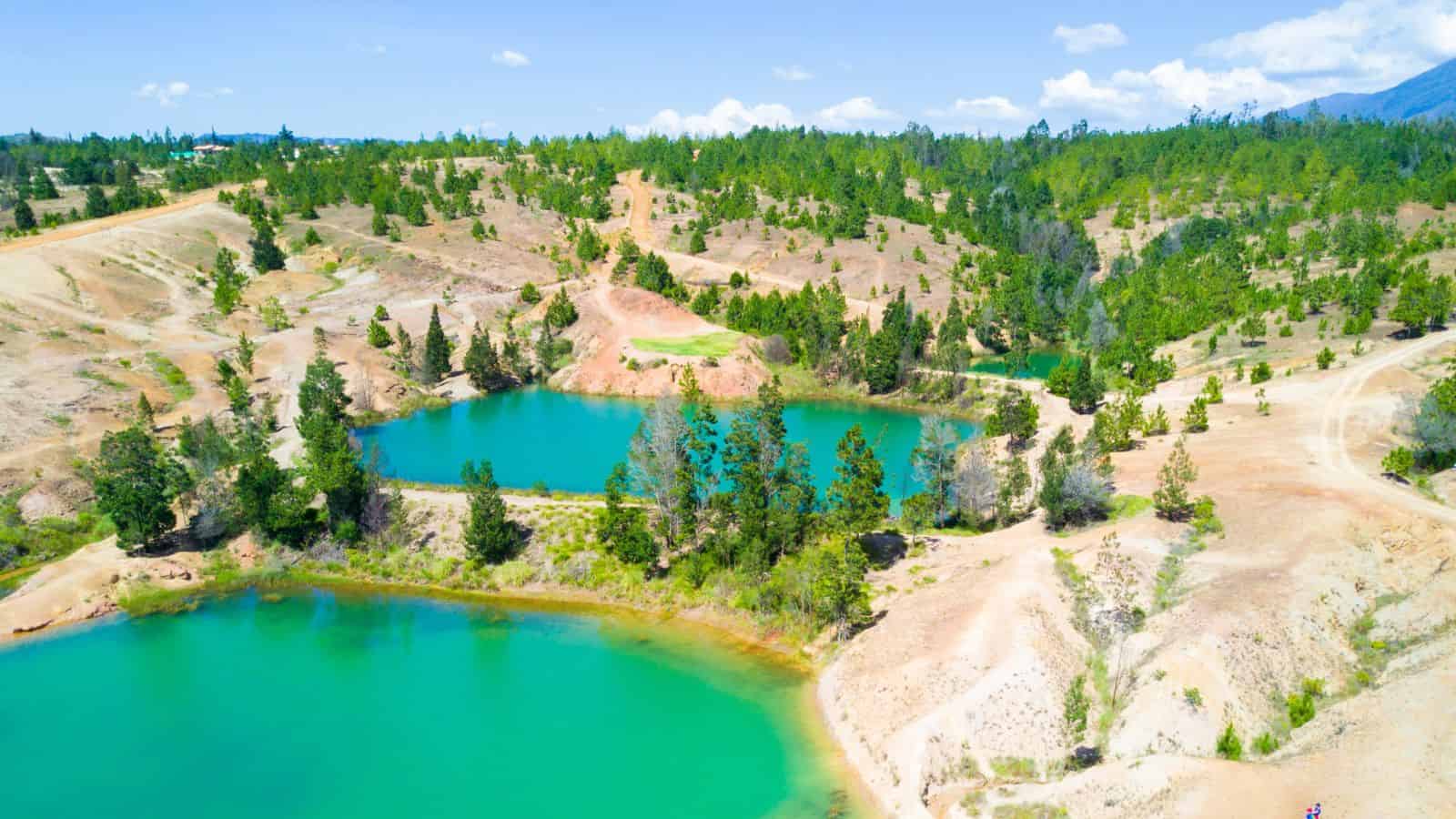 Aerial view of turquoise lakes surrounded by trees and dry, rocky hills under a blue sky.