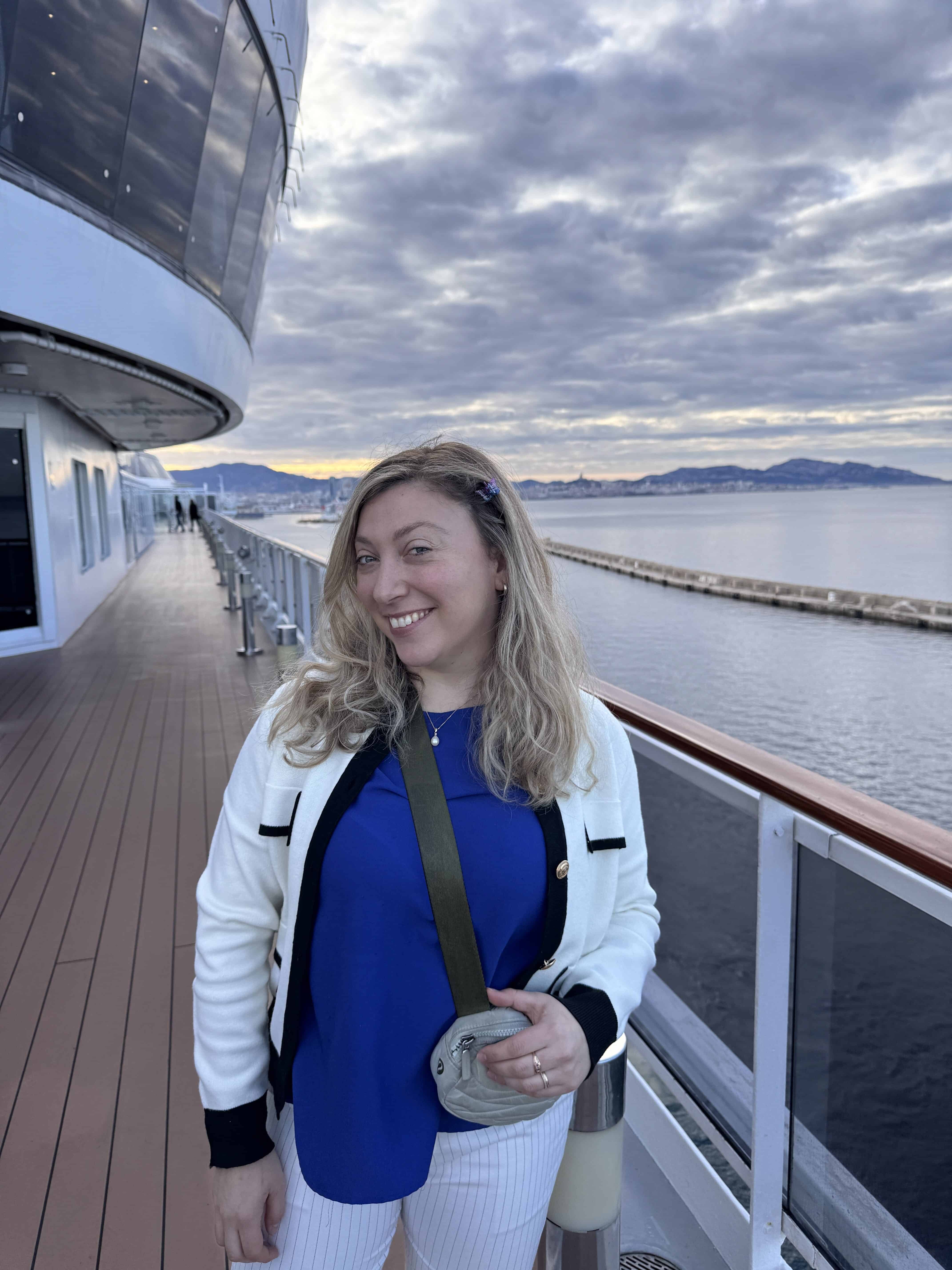 Woman smiling on a ship deck with mountains and a cloudy sky in the background, enjoying her Family Cruise aboard MSC Fantasia.