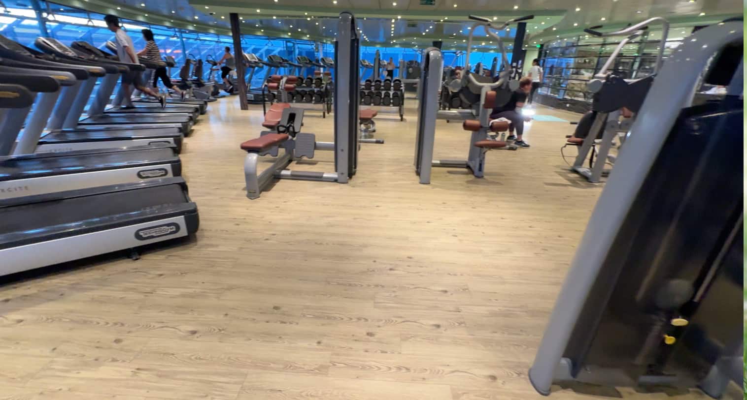 A spacious gym aboard MSC Fantasia with treadmills, weight machines, and people exercising on a wooden floor—perfect for your 2025 cruise review.