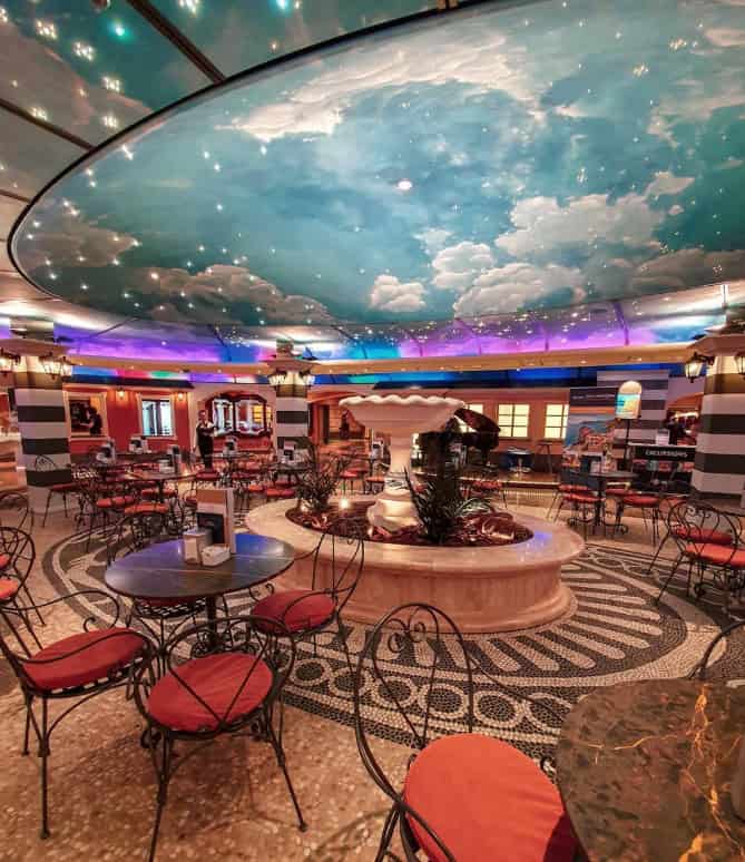 Cafe with round tables and red chairs, a fountain centerpiece, and a ceiling painted like a sky with clouds, inspired by the elegant ambiance of MSC Fantasia Dining.