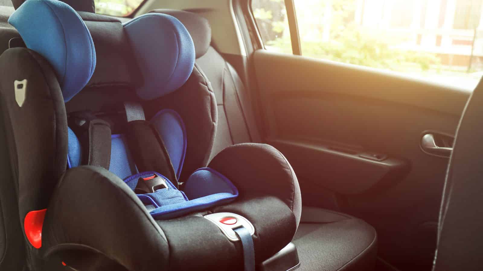 A blue and black child car seat is installed in the back seat of a car with sunlight coming through the window.
