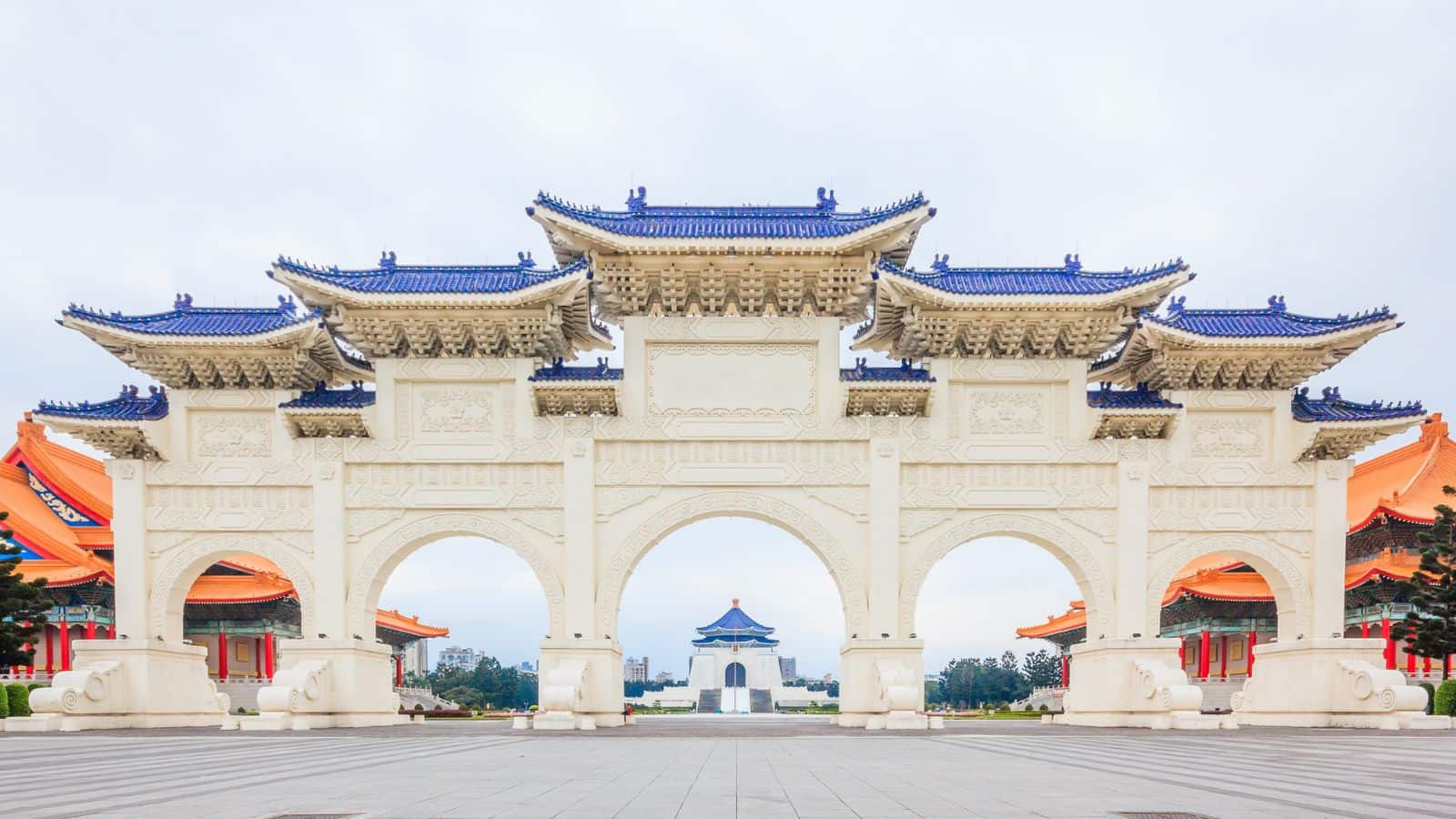 A large traditional Chinese gate with blue tiles, leading to a monument and flanked by orange-roofed buildings.