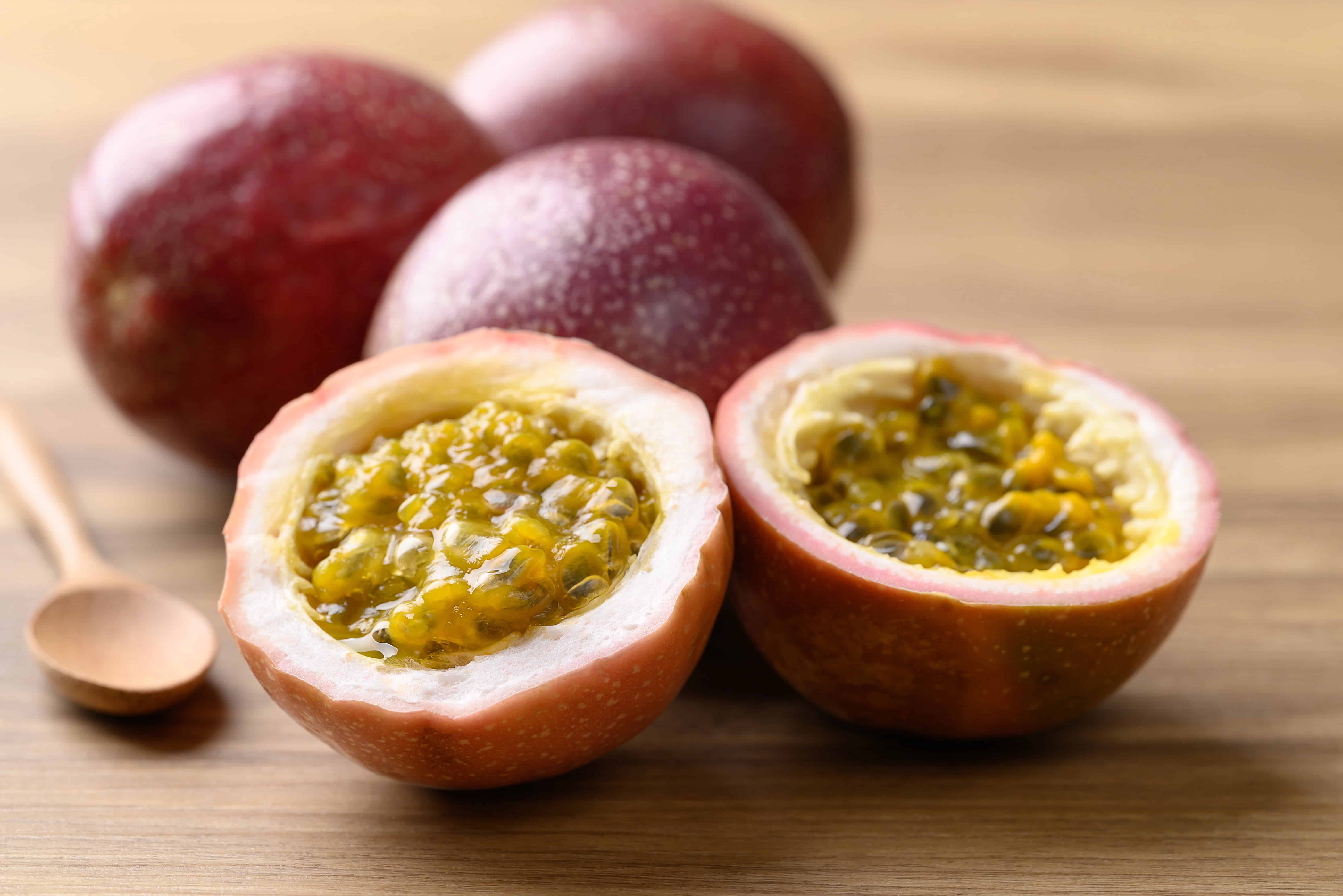 Halved passion fruit showing yellow pulp, with whole exotic Colombian fruits and a wooden spoon in the background.