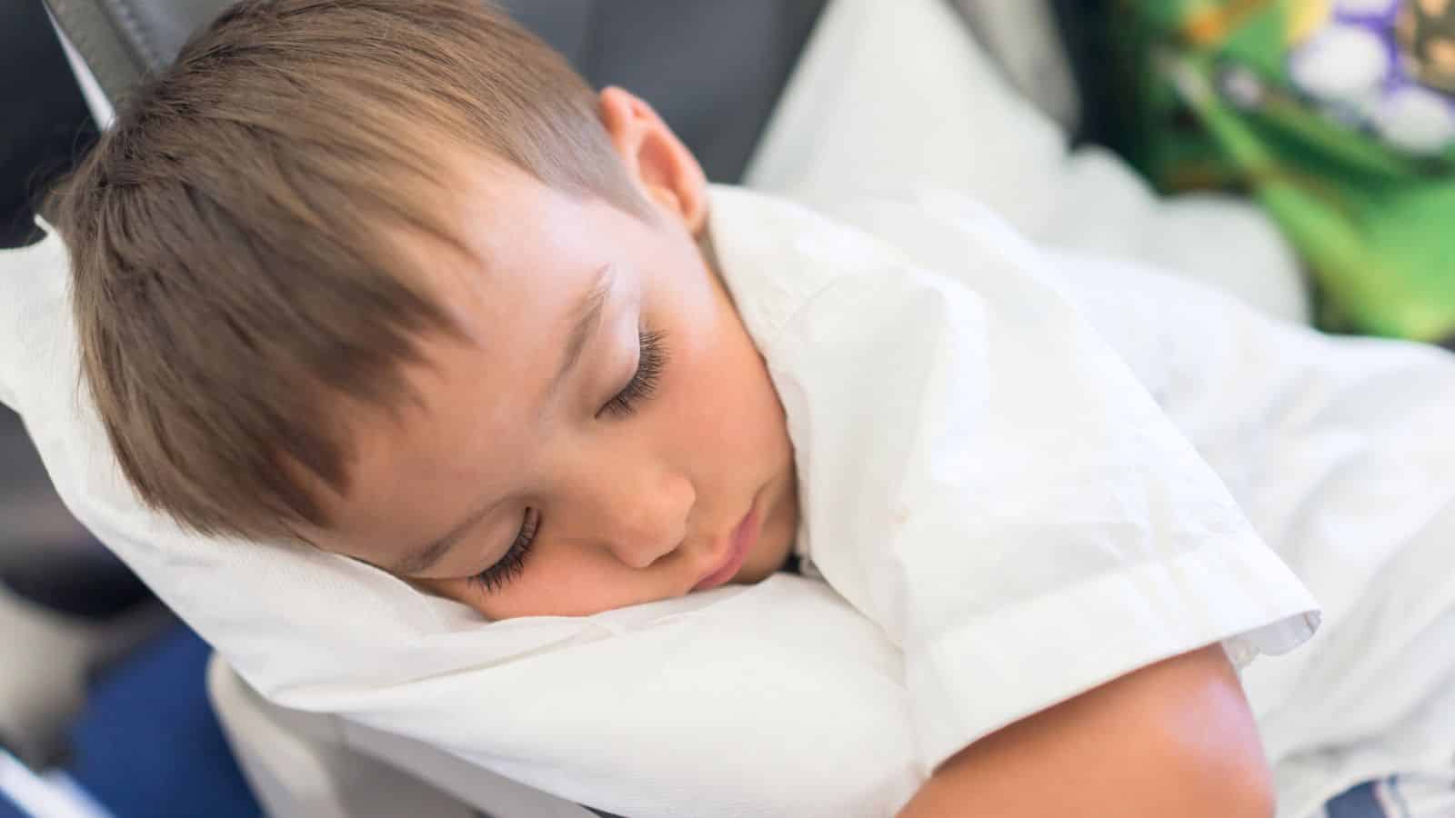 Young boy sleeping on a white pillow, resting his head while wearing a white shirt.