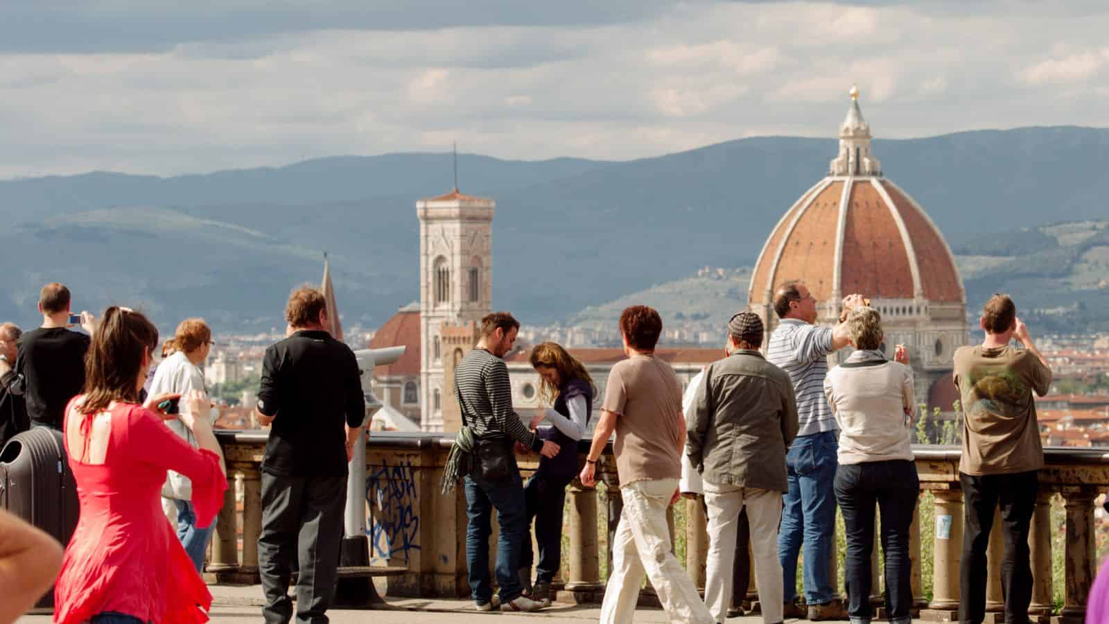 Tourists take photos of Florence&rsquo;s Duomo and bell tower from a scenic overlook on a sunny day.