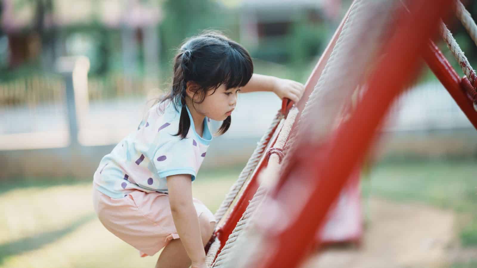 Young girl climbing a rope structure at a playground, focused and determined, with a blurred background.