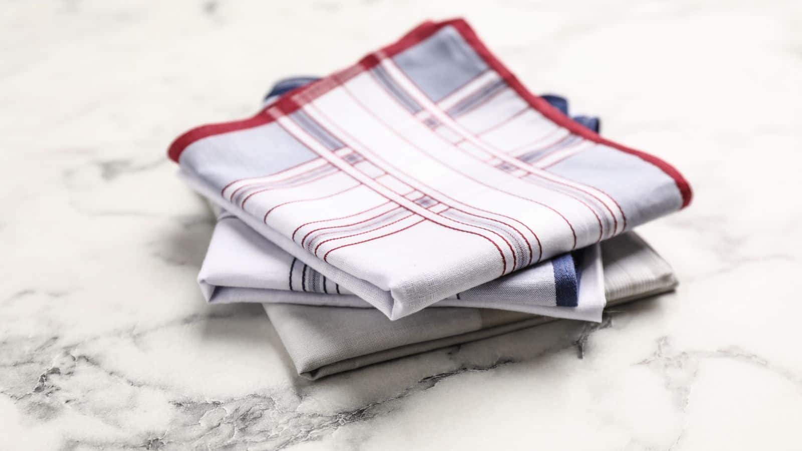 Three folded handkerchiefs with red and blue stripes stacked on a white marble surface.