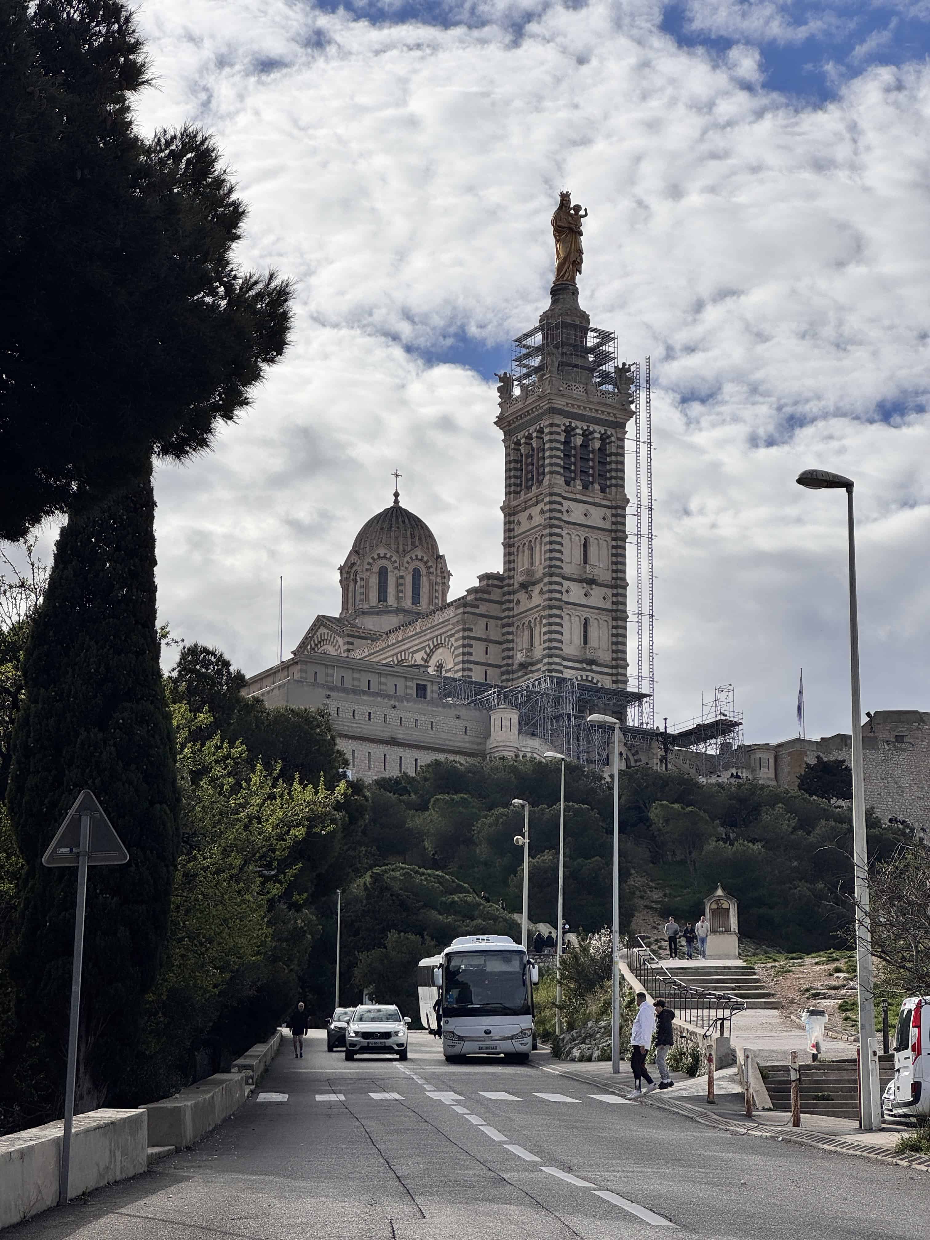 View of Notre-Dame de la Garde basilica on a hill in Marseille, France, with vehicles and people on the street below—a must-see stop on any Marseille itinerary.