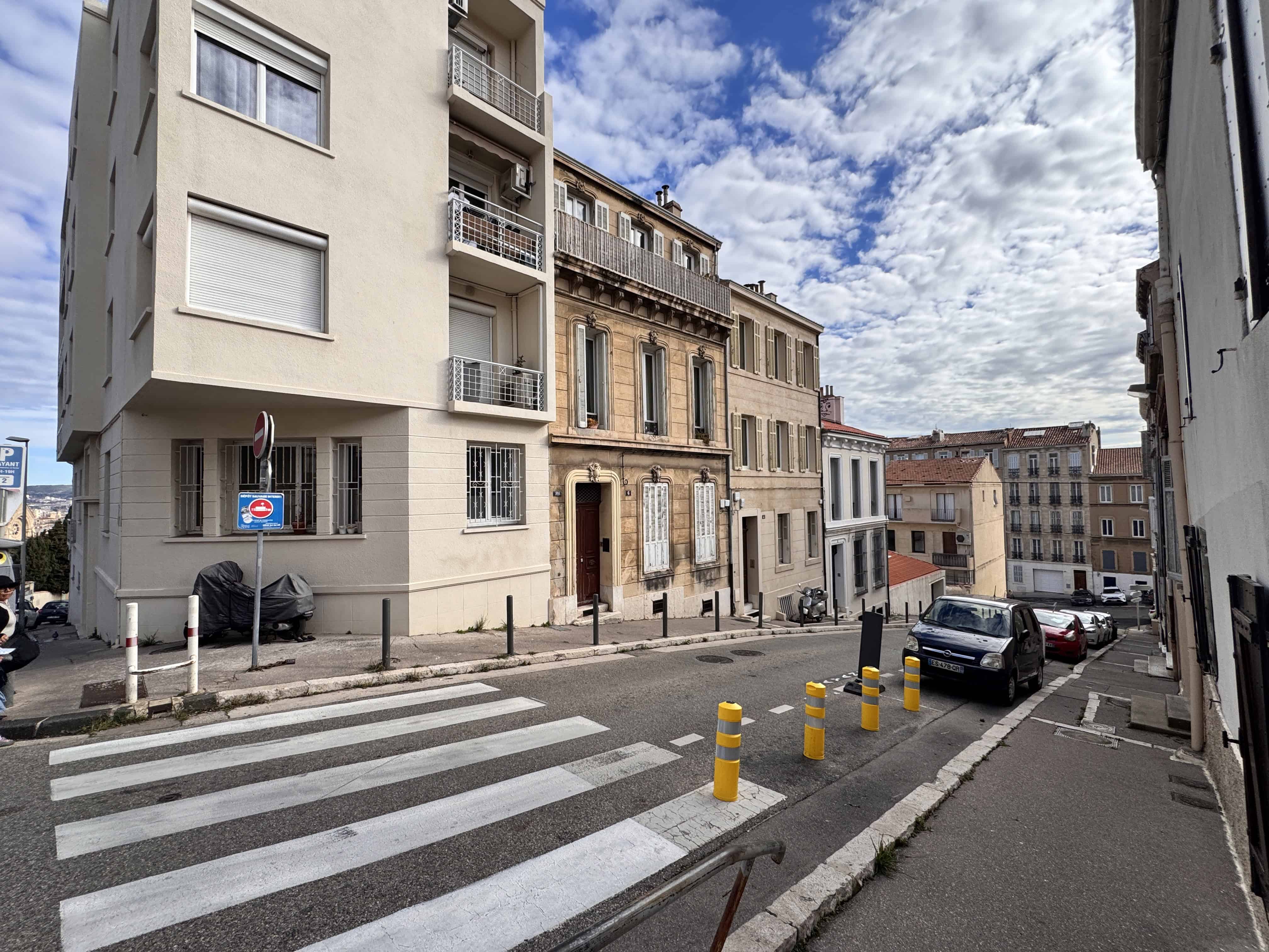 A crosswalk on a sloped street lined with apartment buildings under a partly cloudy sky.