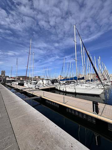 Sailboats are docked at a marina under a blue sky with scattered clouds.