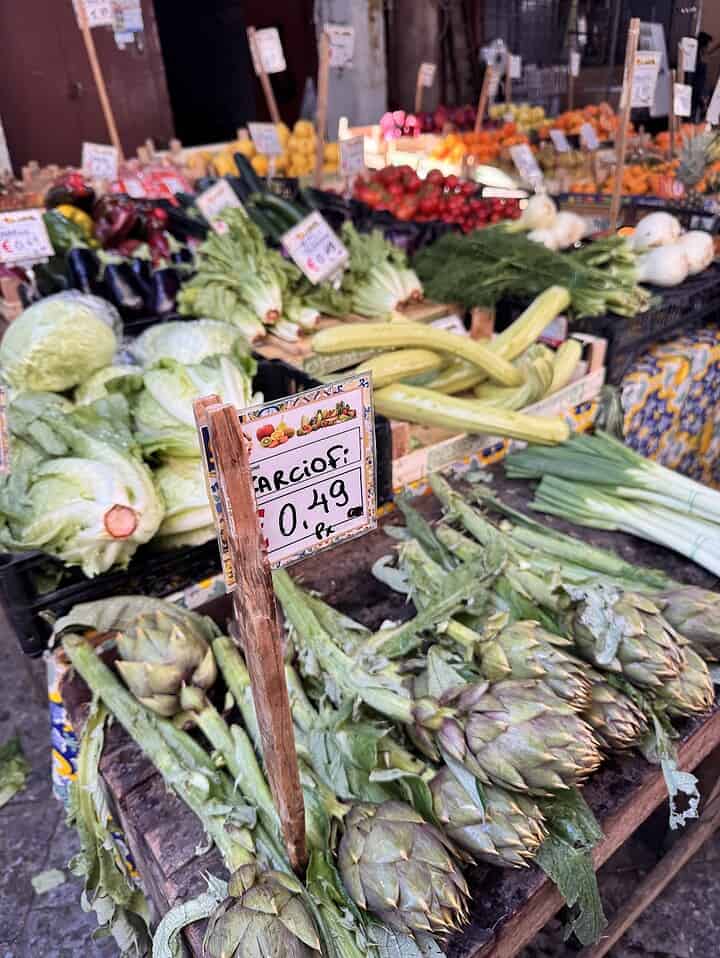 Fresh vegetables including artichokes, lettuce, and onions on display at an outdoor market stand.