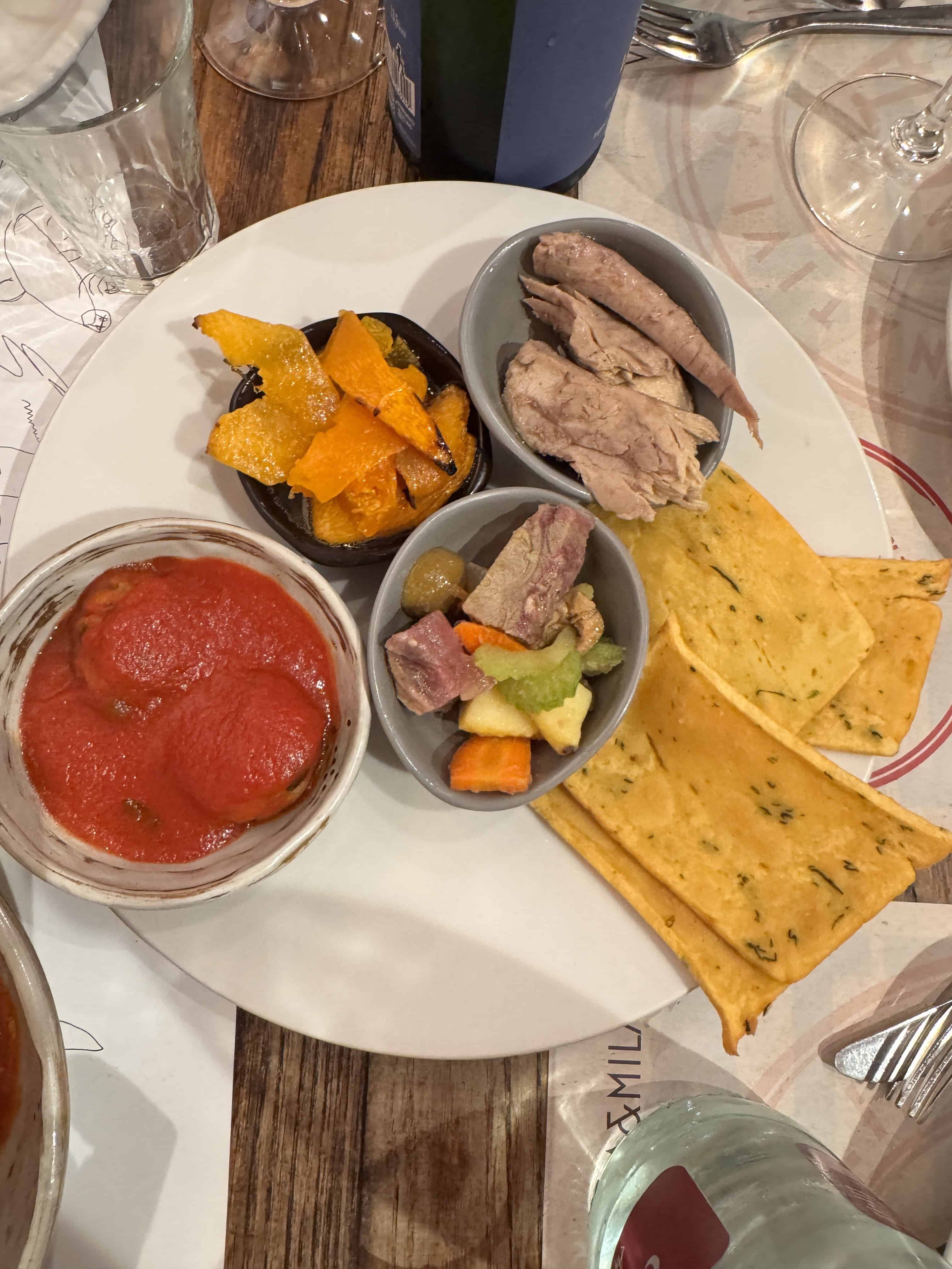 A plate with focaccia, chicken, vegetables, roasted squash, and a bowl of tomato sauce&mdash;perfect inspiration if you&rsquo;re wondering what to do in Palermo for a day and want to savor authentic local flavors.