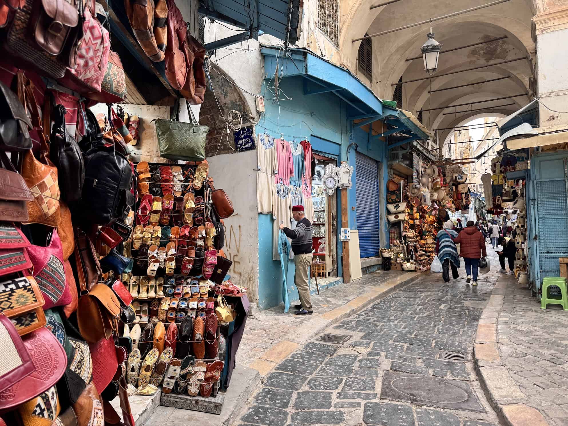 Narrow market street with colorful goods, shoes, and bags displayed; people walking and shopping, much like the bustling ports you might visit with helpful first time cruise tips in mind.
