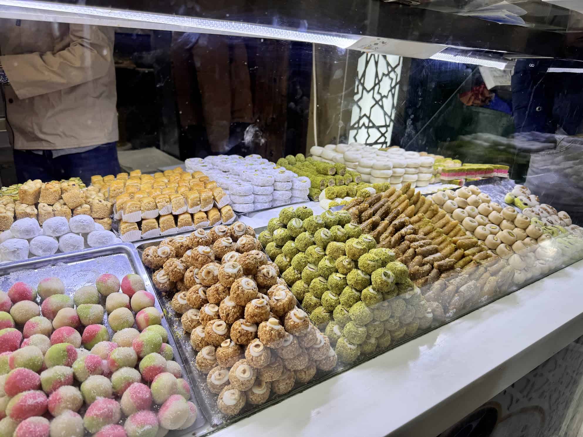 A display case filled with assorted colorful Middle Eastern sweets and pastries in a shop.