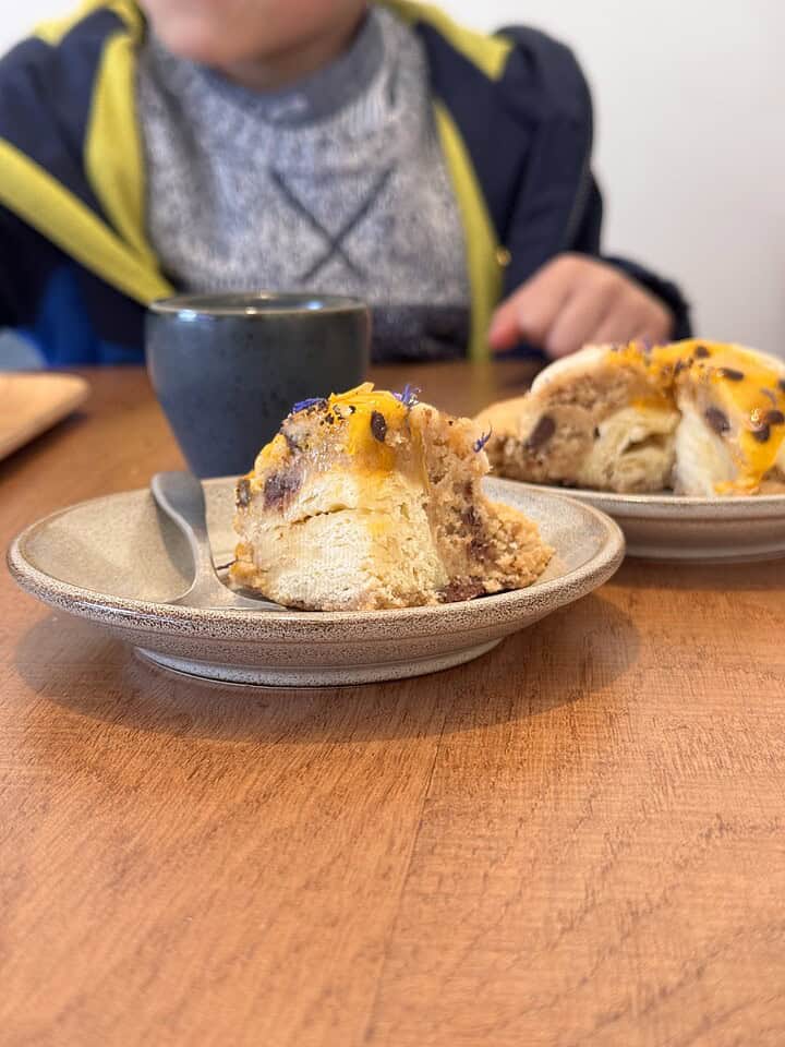 A child sits at a table with two dessert pastries and a cup, ready to eat.