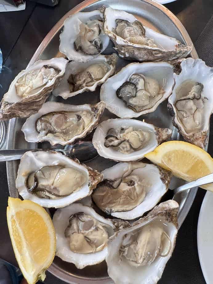 A platter of fresh oysters on the half shell with lemon wedges and small forks, just like those found in Barcelona markets&mdash;perfect for anyone seeking where to eat the finest fresh food.
