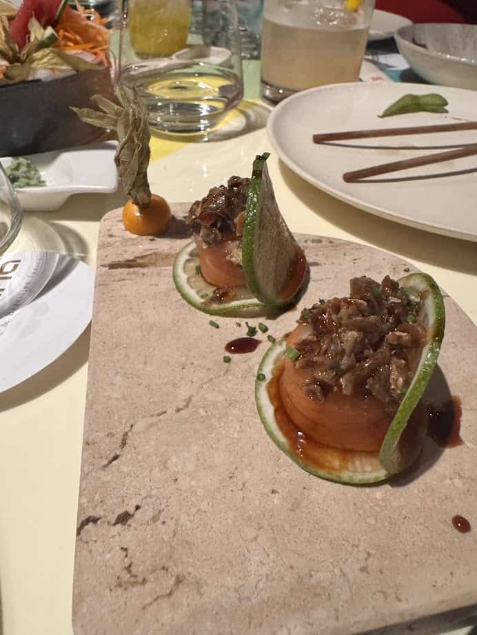 A gourmet appetizer with sliced lime, tomato, and garnish on a marble slab captures the vibrant spirit of fresh food found in Barcelona markets, set alongside drinks and other dishes for an authentic tasting experience.