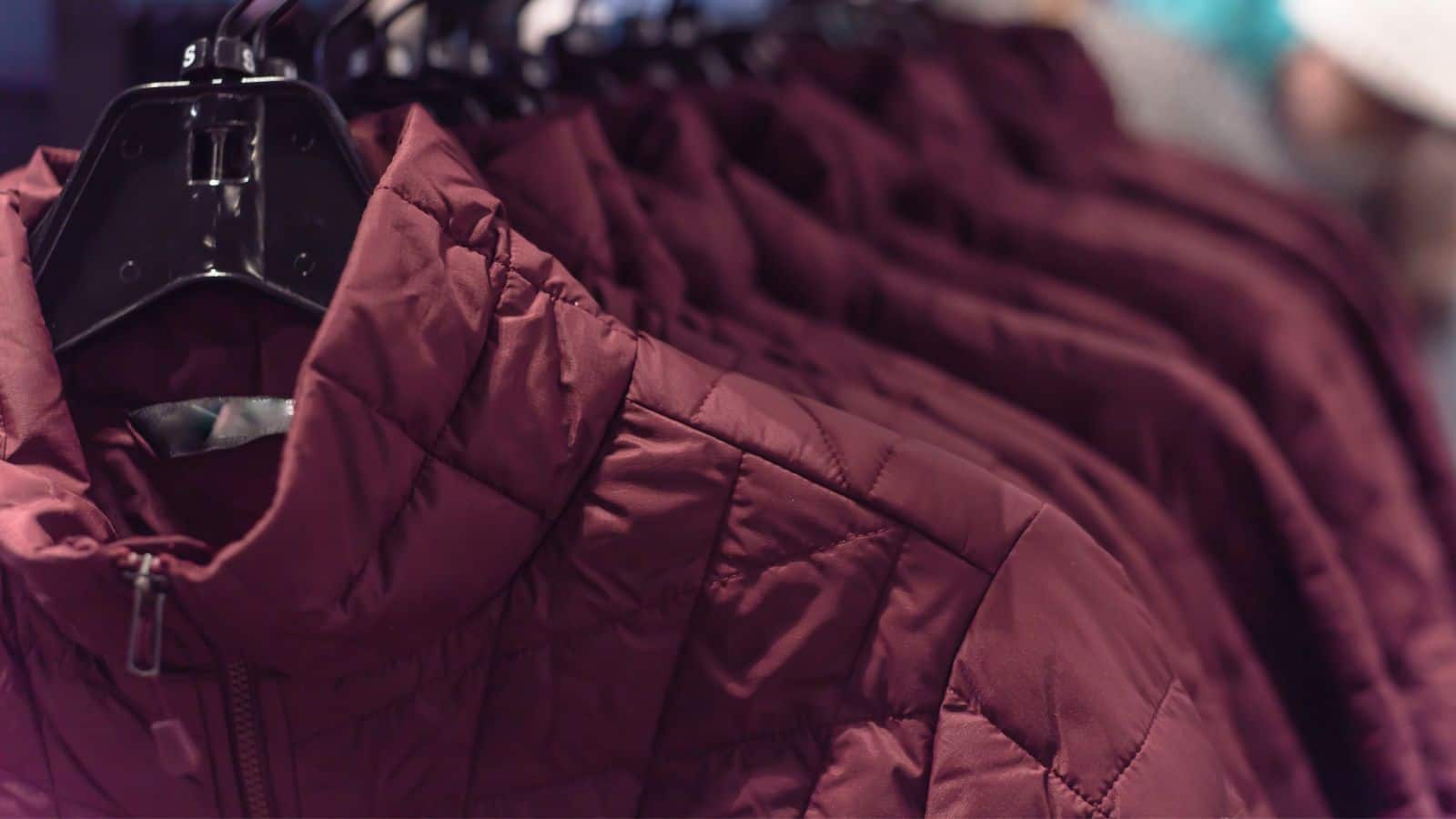 Several maroon quilted jackets hanging on black plastic hangers in a row on a clothing rack.