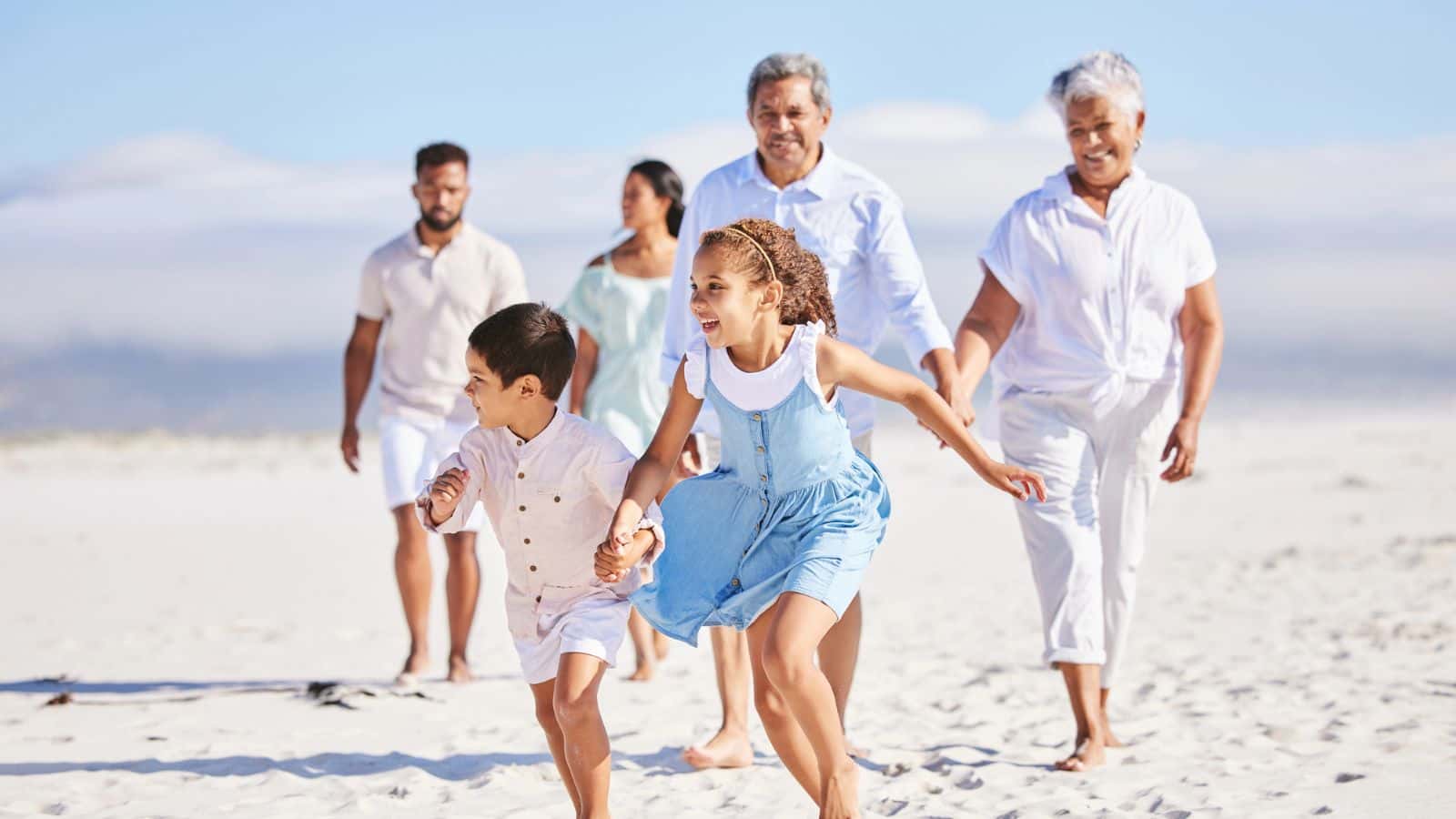 Family of six, including children and elders, walking and smiling together on a sunny beach.