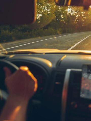 Driver’s view inside a car on a winding road at sunset, sunlight shining through the windshield.