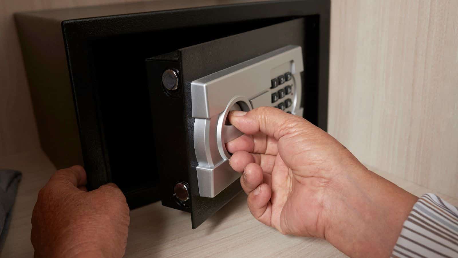 A person’s hands opening a digital safe using the dial inside a wooden cabinet.