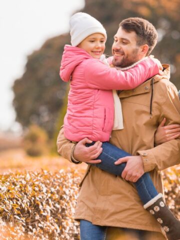 A family of three walks outdoors in autumn, smiling and enjoying the fall scenery.