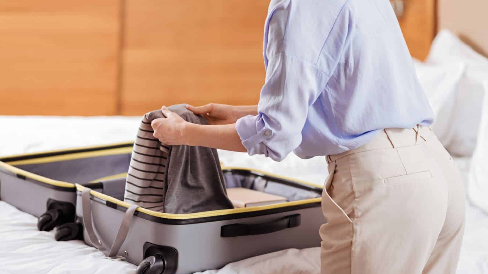 Person packing a striped shirt into an open suitcase on a bed.